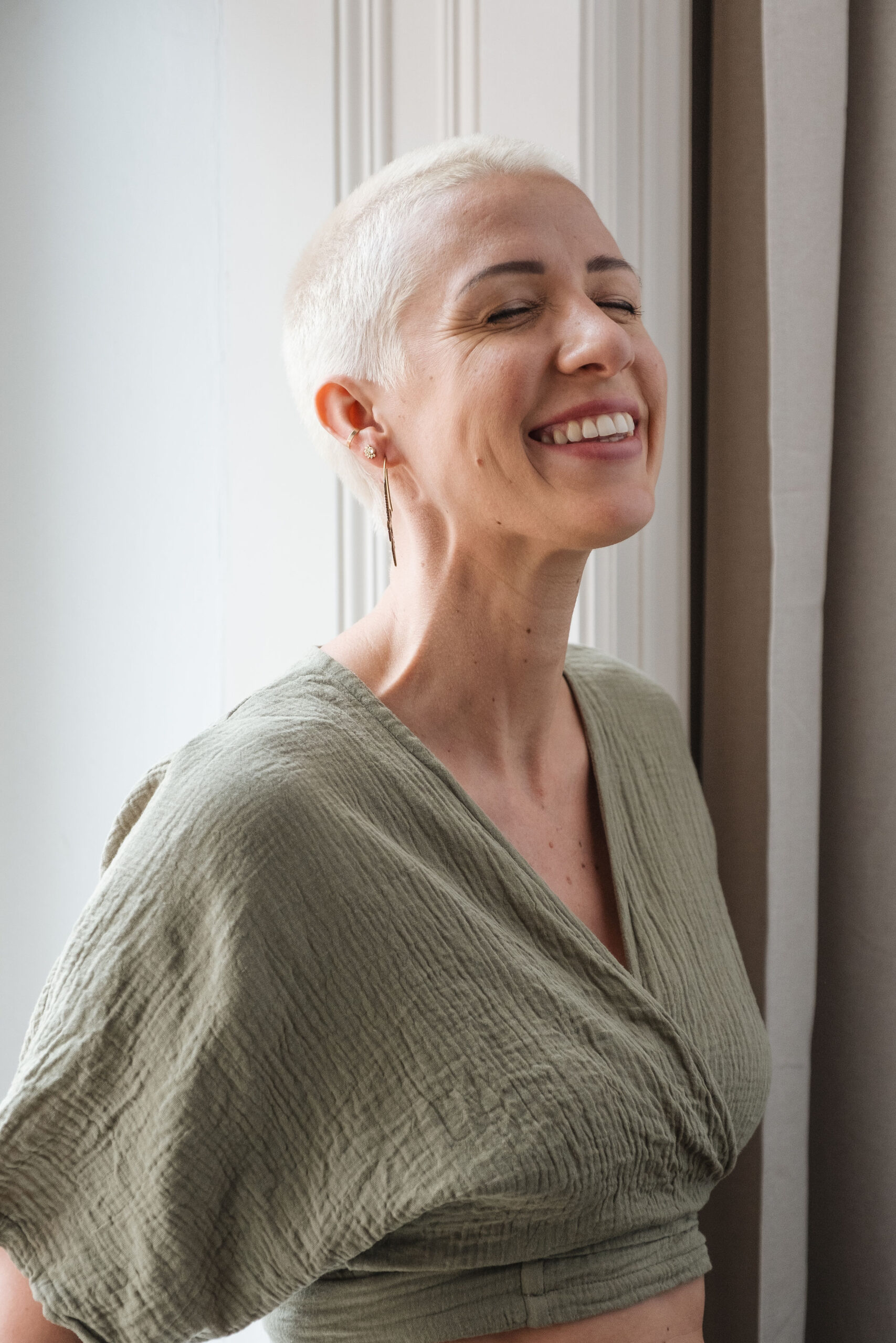 Frau mit kurzem Haar steht am Fenster und lächelt voller Lebensenergie