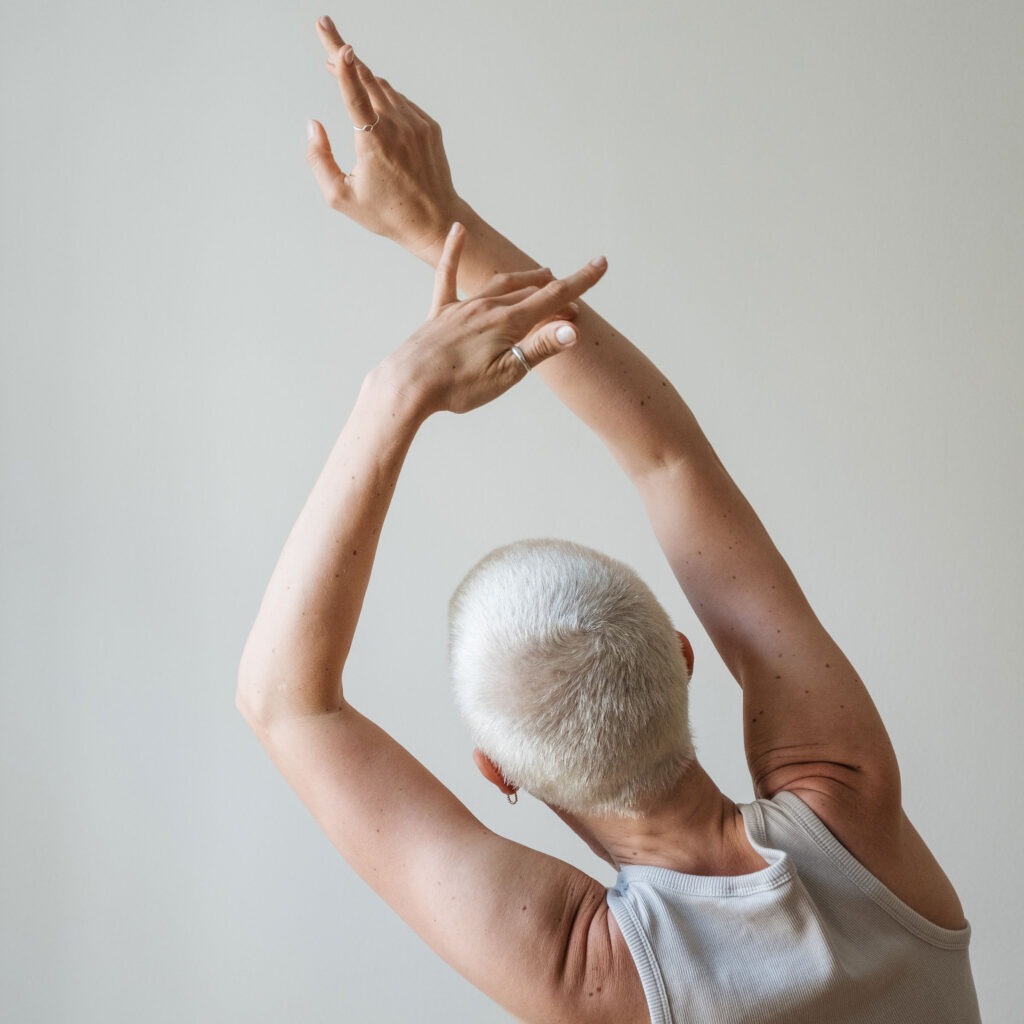 Rückansicht einer Frau, die Arme achtsam über den Kopf streckt